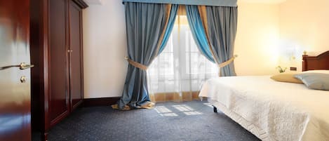 A hotel room with a bed, a wardrobe, and a window with curtains.