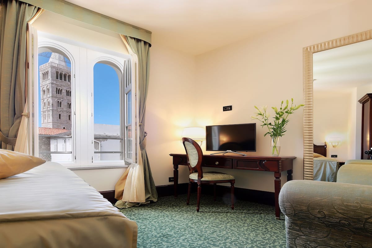 Une chambre d’hôtel avec deux lits, un bureau avec une télévision, une chaise, un vase de fleurs et un grand miroir.