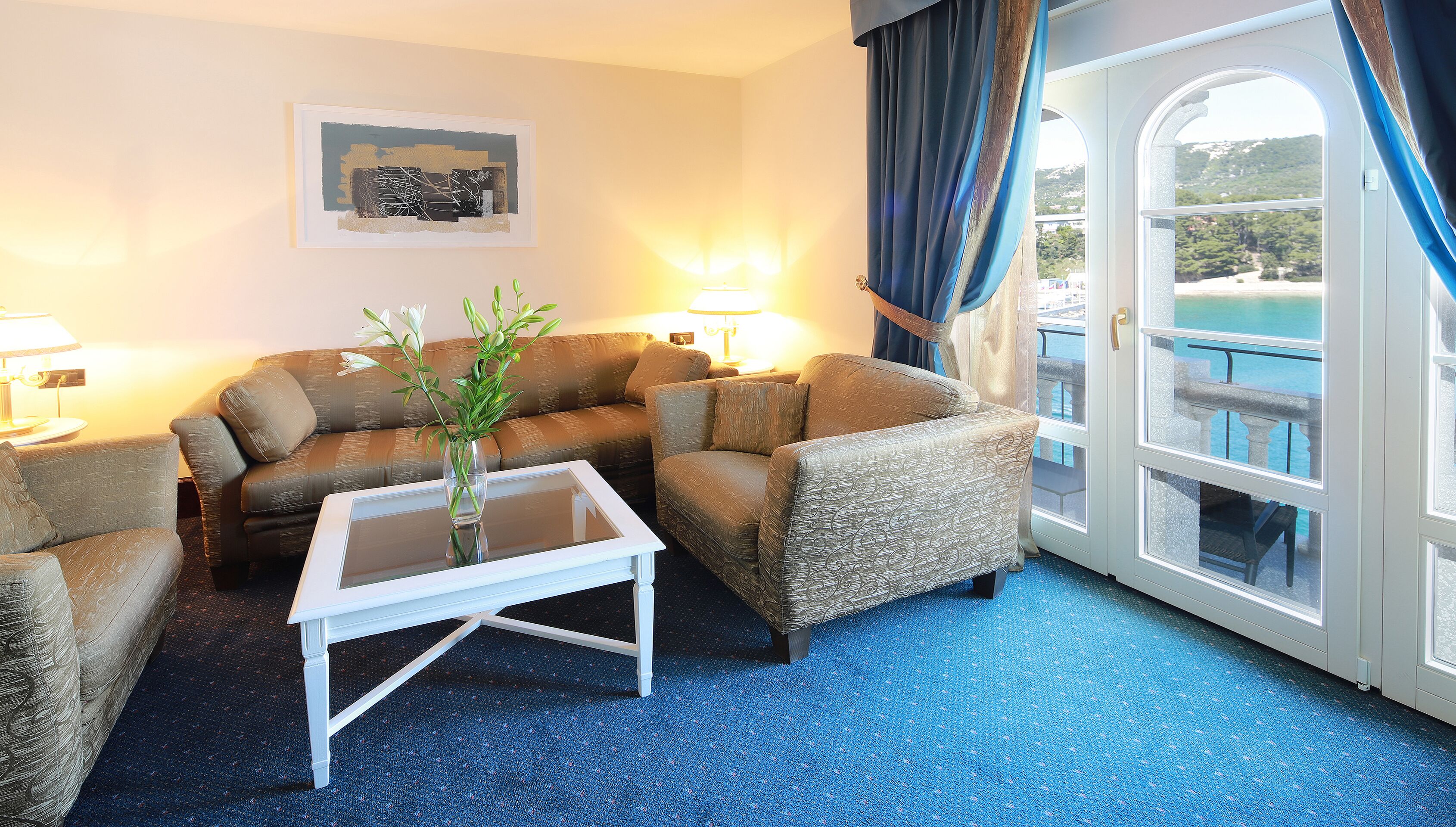 A cozy room with a sofa, armchairs, a coffee table, and a view of the sea through a large window.