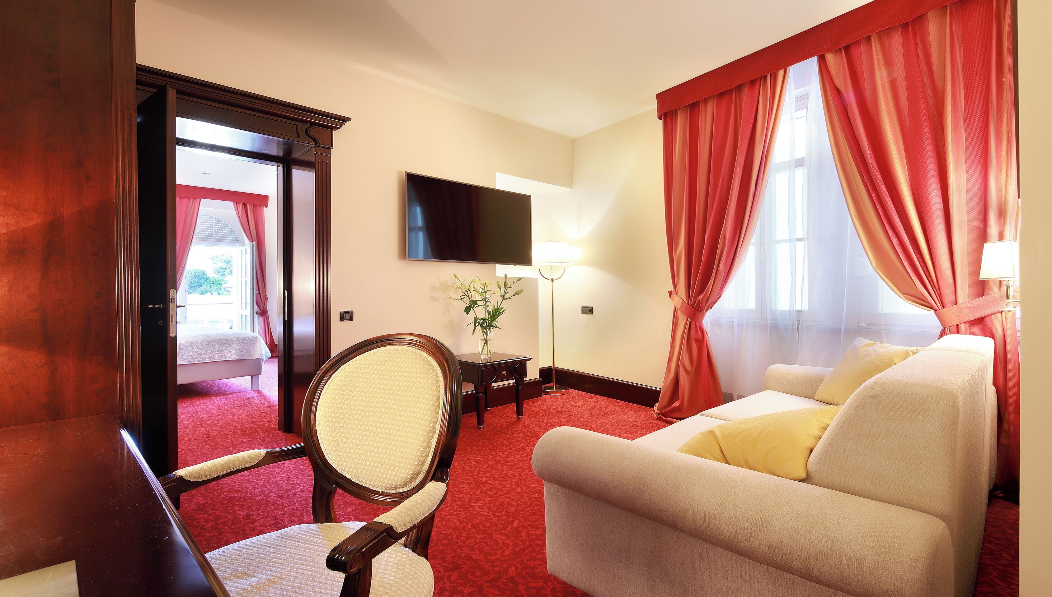 A hotel room with a bed, a sofa, a TV, a lamp, and a window with curtains.
