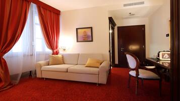 A room with a beige sofa, a wooden chair, a red carpet, a door, and a framed picture on the wall.