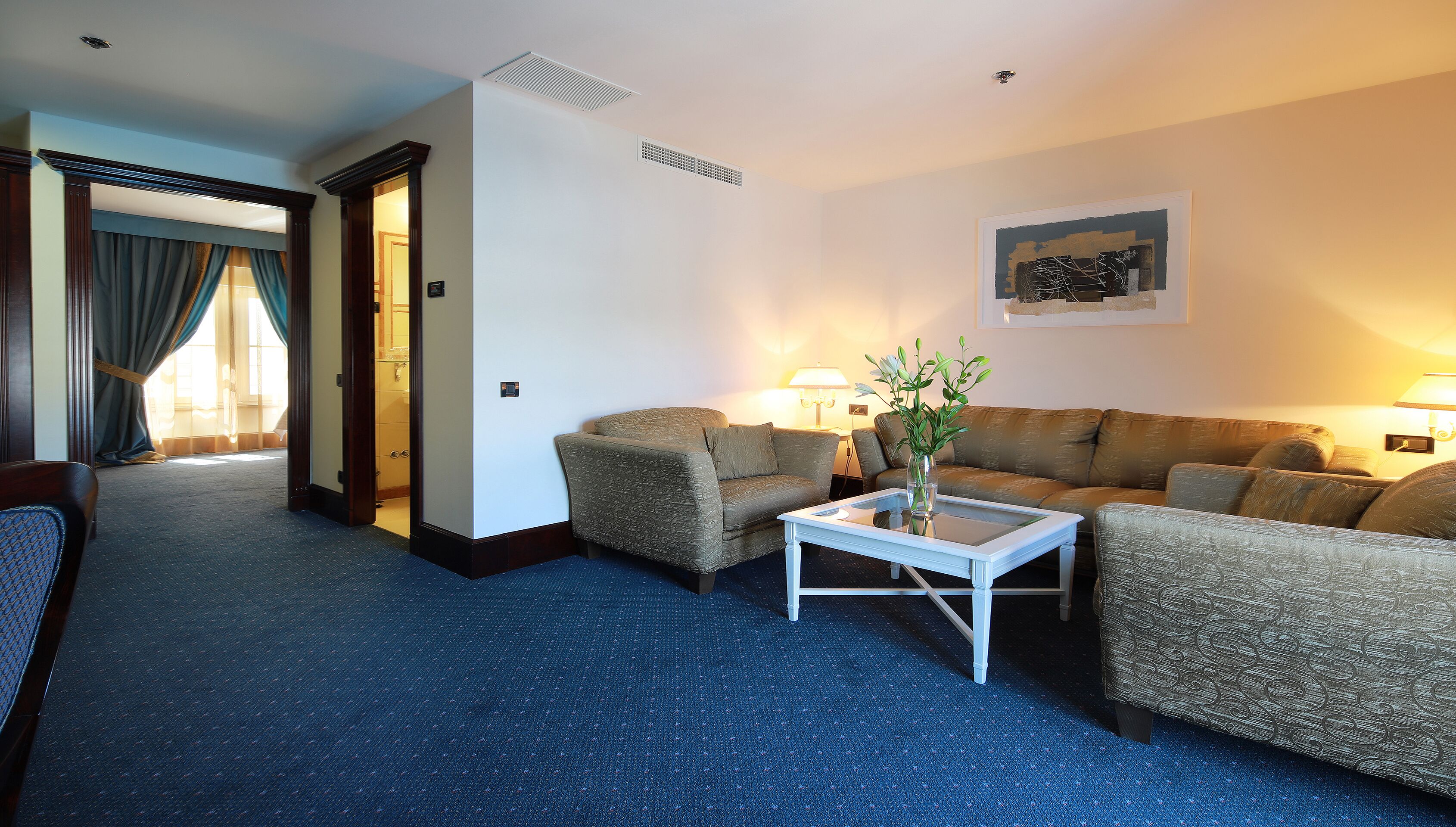 A hotel room with a blue carpet, two sofas, a coffee table, and a lamp.
