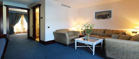A hotel room with a blue carpet, two sofas, a coffee table, and a lamp.