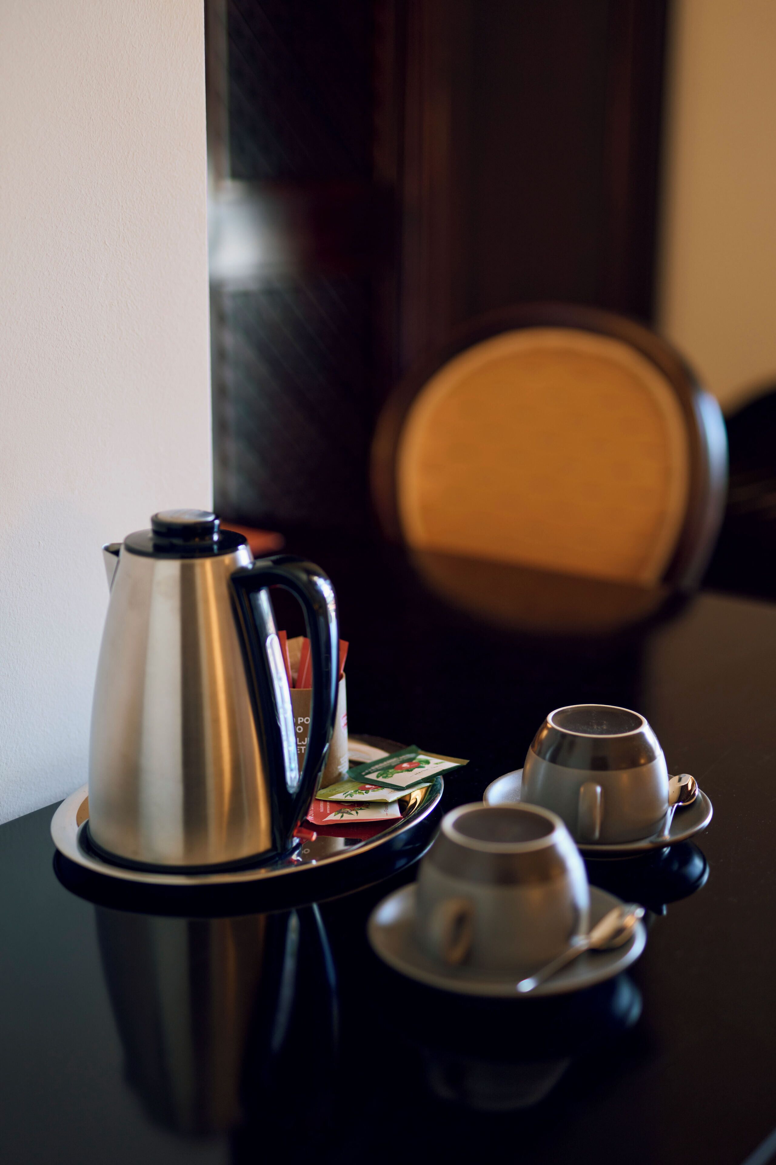 Angolo caffè con caffettiera, tazze e piattini su una superficie riflettente.