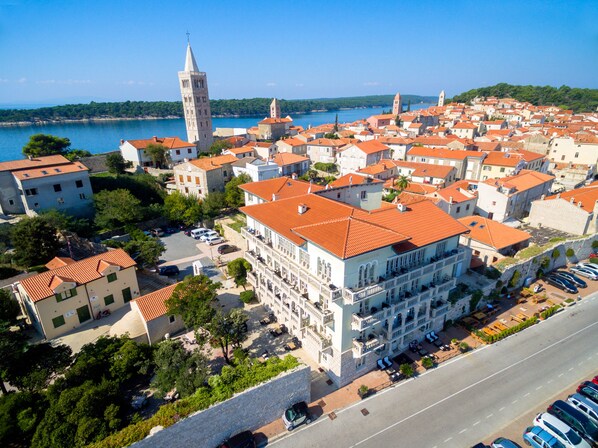 A coastal town with a prominent tower, red-roofed buildings, and a marina. - Arbiana Heritage Hotel (Rab)