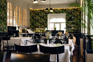 A restaurant with round tables, black chairs, and a green leafy wall. - Arbiana Heritage Hotel (Rab)