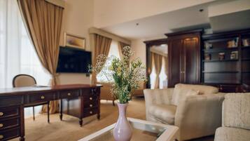A living room with a wooden desk, a beige sofa, and a purple vase with flowers on a glass coffee table.