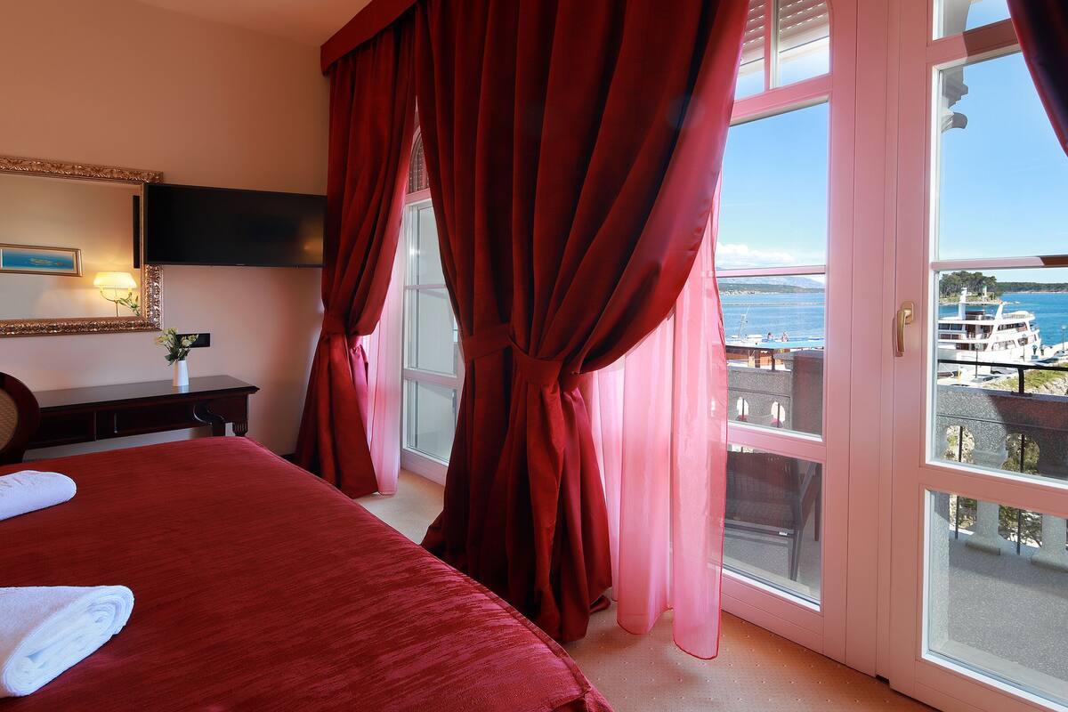 Une chambre d’hôtel avec un lit, un bureau, une lampe et une vue sur la mer, grâce à de grandes fenêtres.
