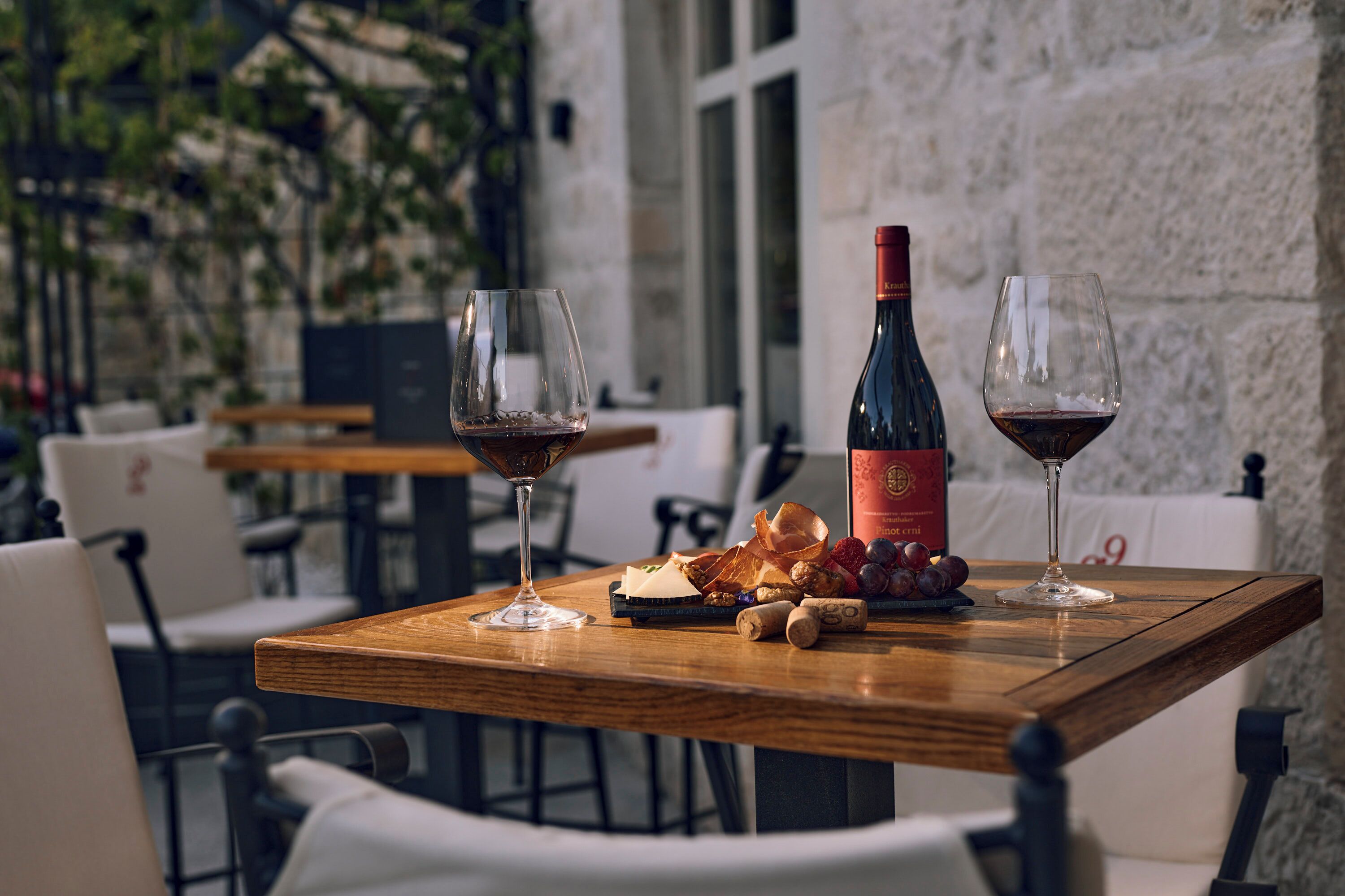 A wooden table with two wine glasses, a bottle of wine, and a plate of snacks.