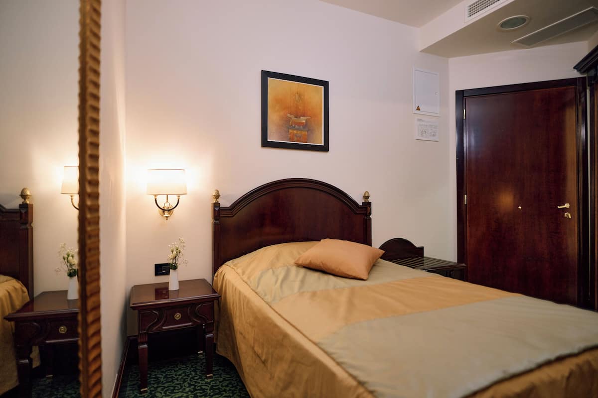 Une chambre d’hôtel avec un lit en bois, des lampes de chevet, un tableau encadré au mur et une porte.