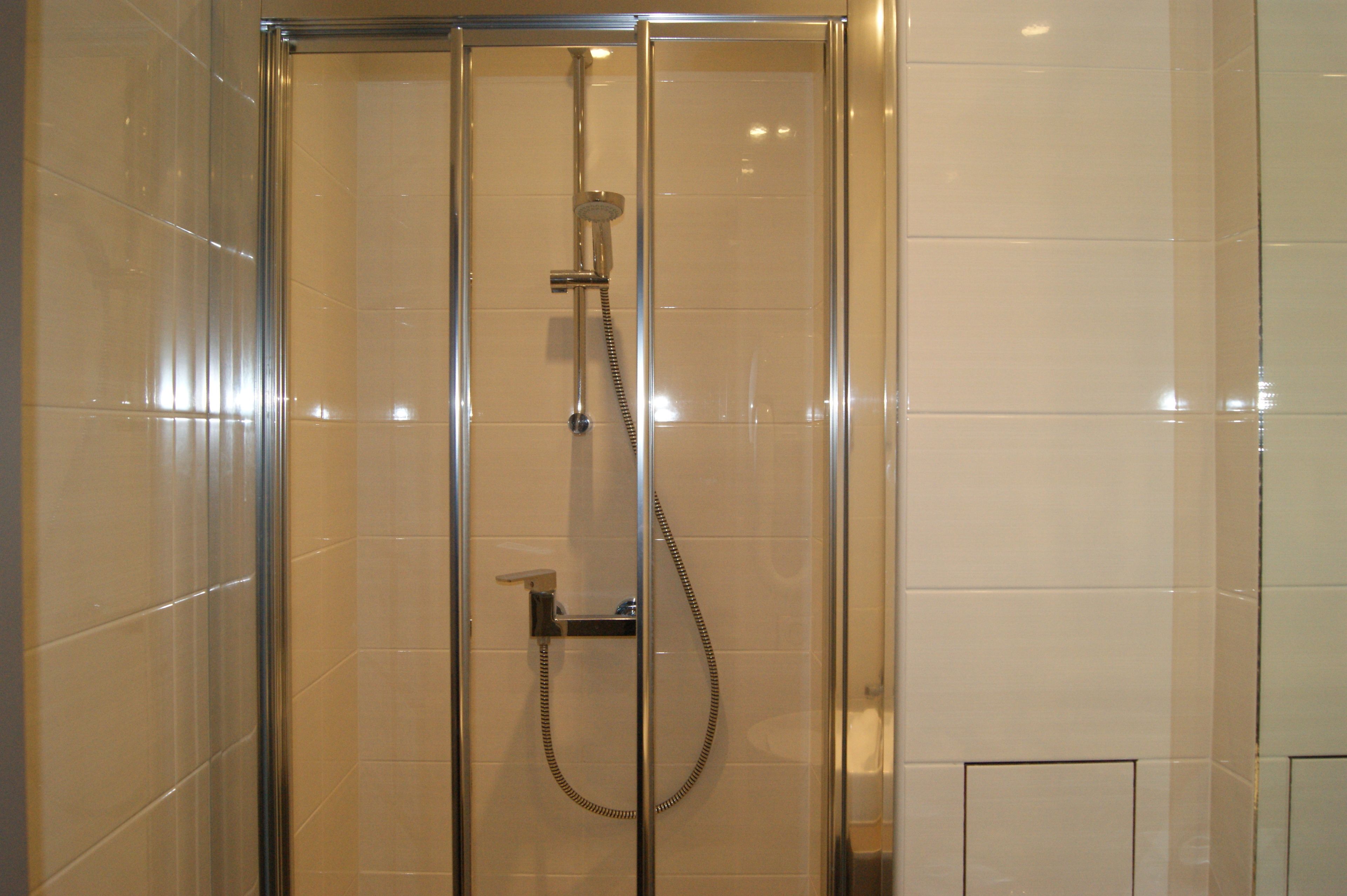 A glass-enclosed shower with a handheld showerhead and a wall-mounted faucet.