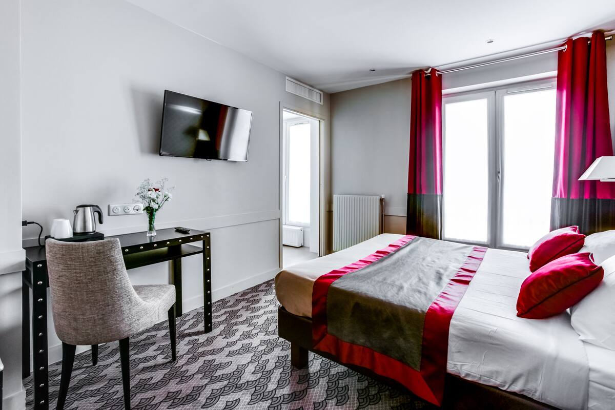 Ein Hotelzimmer mit Bett, Schreibtisch, Stuhl, Fernseher und einem Fenster mit Vorhängen.