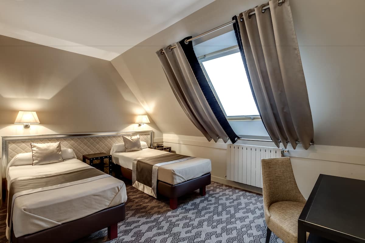 Ein Hotelzimmer mit zwei Betten, einem kleinen Tisch, einem Stuhl und einem Fenster mit Vorhängen.