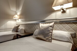 Habitación de hotel con dos camas, una mesita de noche, una lámpara fijada a la pared y un cabecero acolchado.
