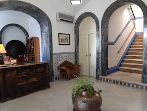 Ein Empfangsbereich mit einem Holztisch, einem Blumentopf und einer Treppe mit blau gefliesten Wänden.