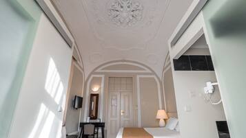 A bedroom with a bed, desk, and chair, a door leading to another room, and a ceiling with decorative molding.
