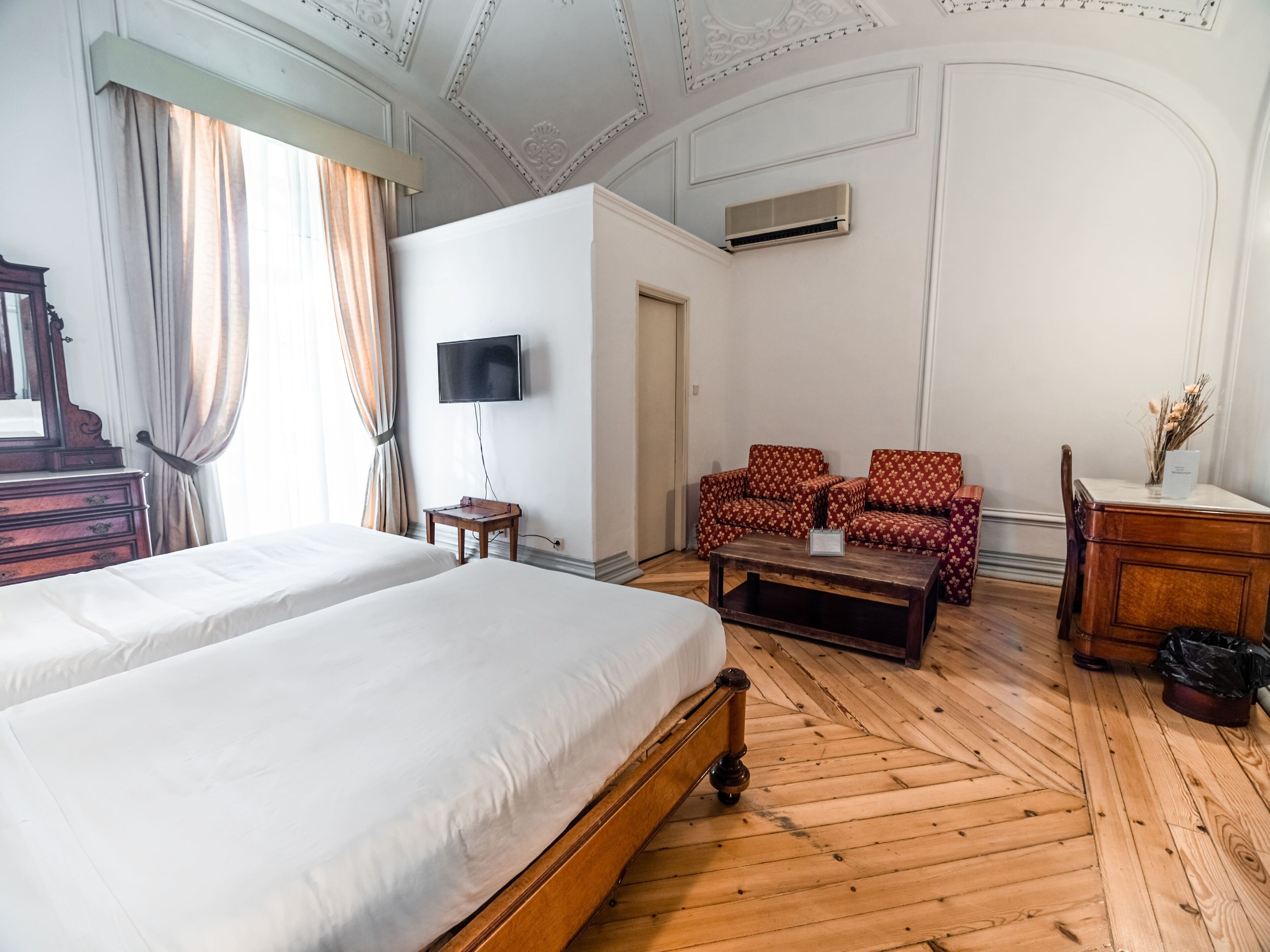 A hotel room with two beds, a sofa, a TV, and a wooden floor.
