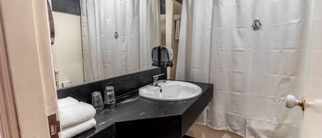 A bathroom with a white sink, black countertop, and a mirror above it. There is a white towel on the counter and a small stool.