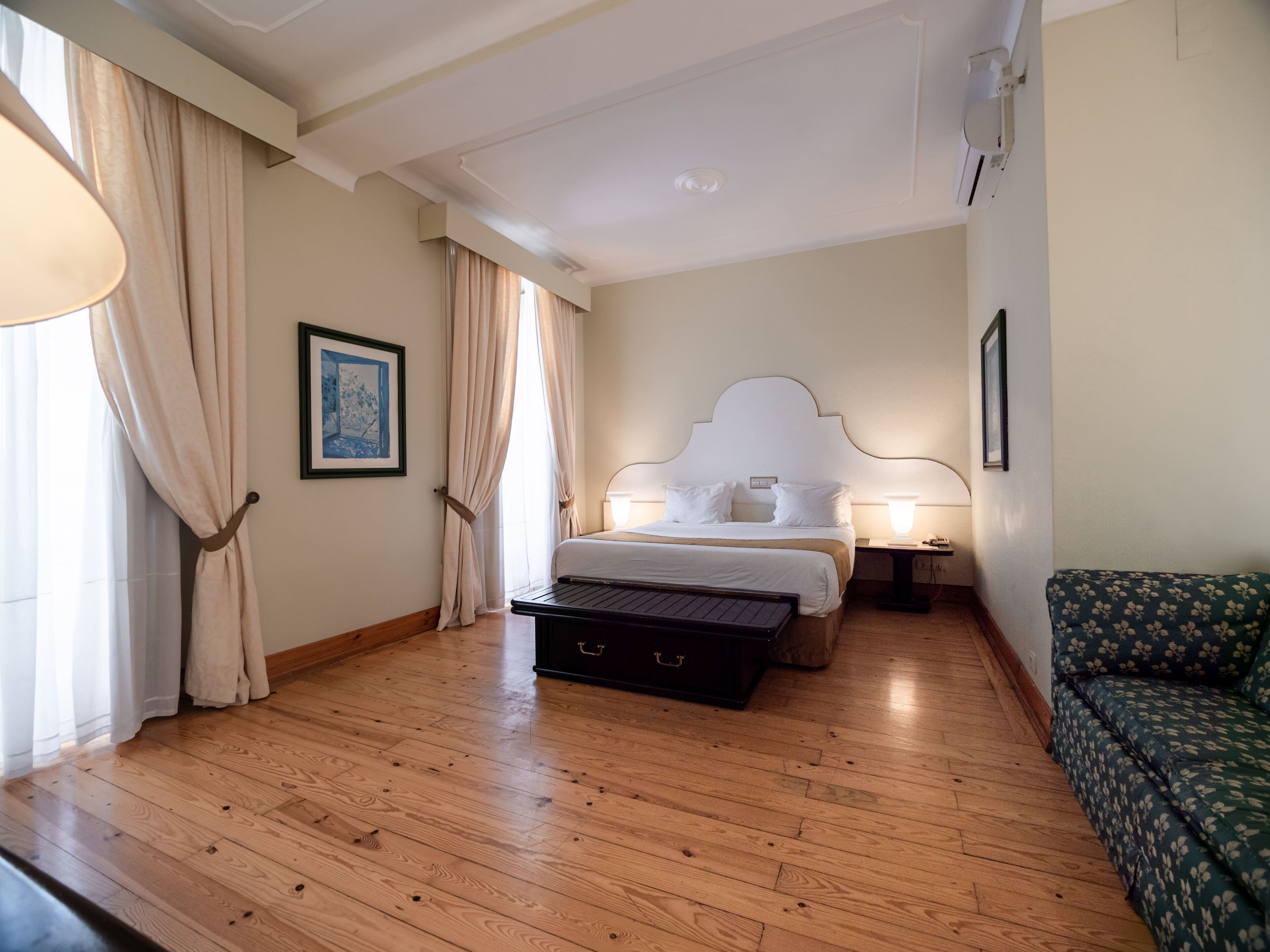 A hotel room with a wooden floor, a bed with white bedding, a green sofa, and a small table.