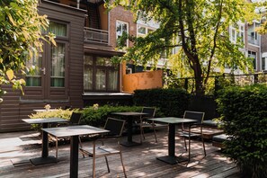 An outdoor patio with tables and chairs, surrounded by greenery and a building with a balcony. - Hotel Roemer (Amsterdam)
