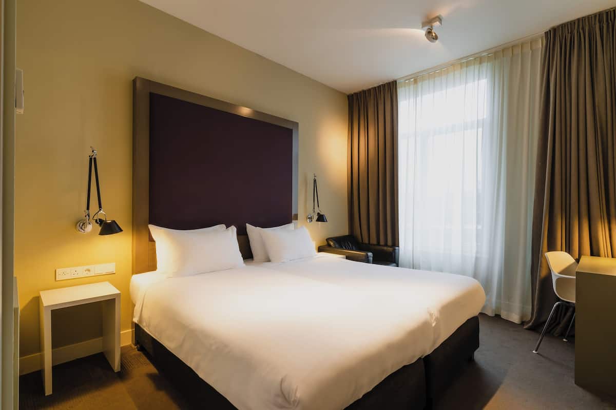 A hotel room with a large bed, bedside tables, a desk, and a chair.