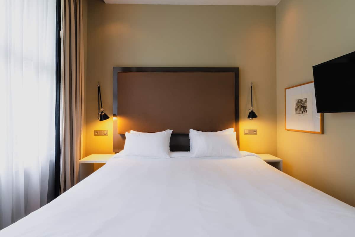 A hotel room with a large bed, two bedside tables, and a mounted television.