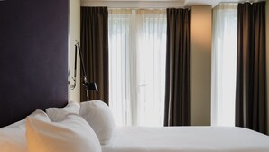 A hotel room with a large bed, a bedside table, and a window with curtains. - Hotel Roemer (Amsterdam)