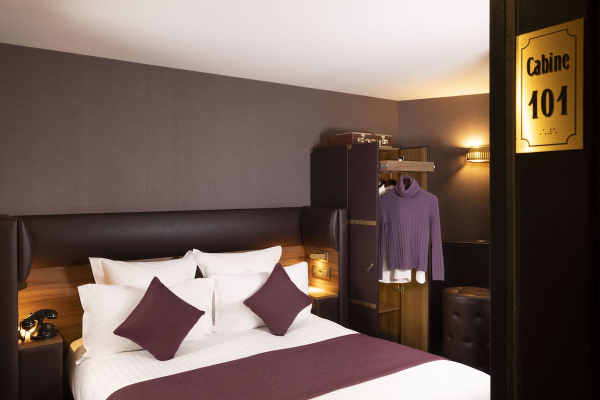 A hotel room with a large bed, a wardrobe, a robe, and a sign indicating the room number.
