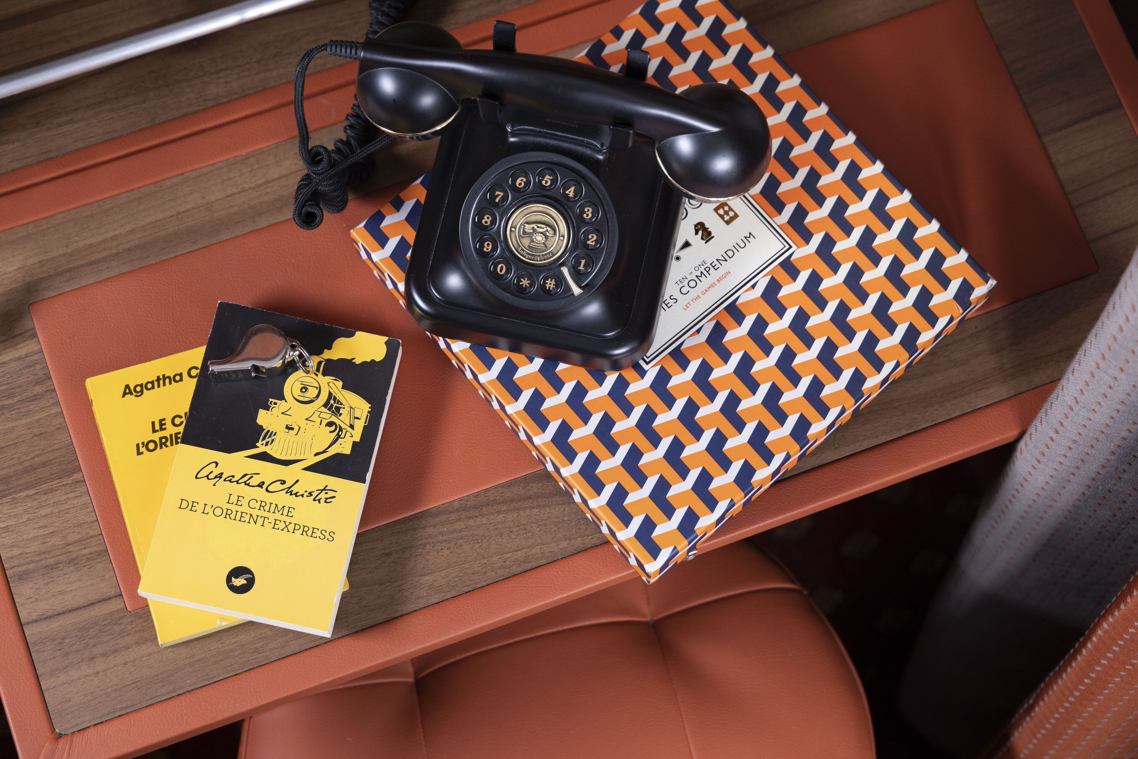 A vintage telephone, a patterned notebook, and a book titled "Le Crime de l'Orient-Express" on a wooden surface.