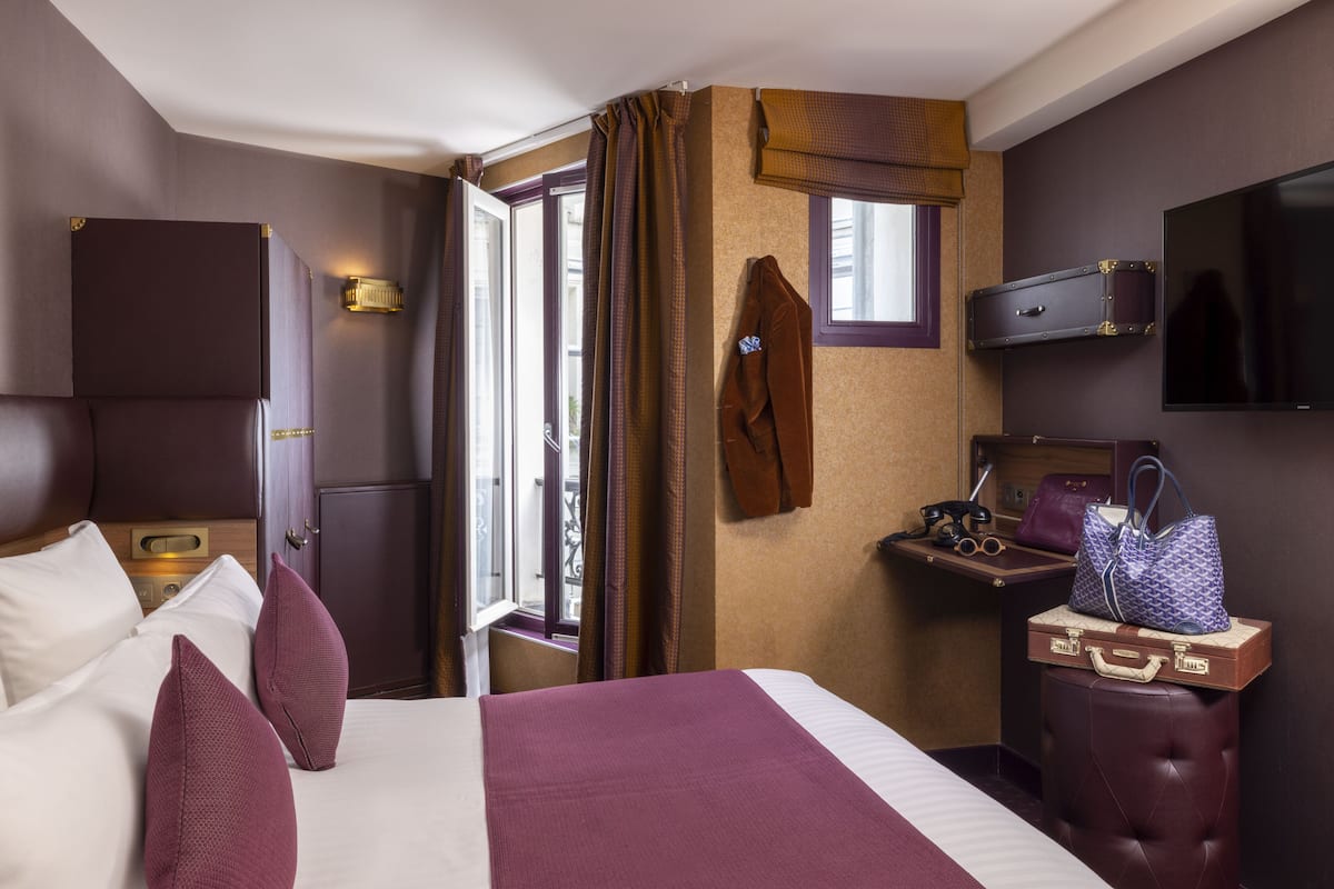 A hotel room with a bed, a desk, a TV, and a window with curtains.