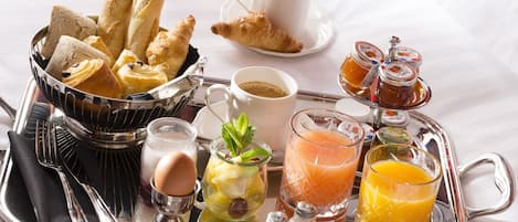 A breakfast tray with croissants, bread, eggs, coffee, juice, and condiments.