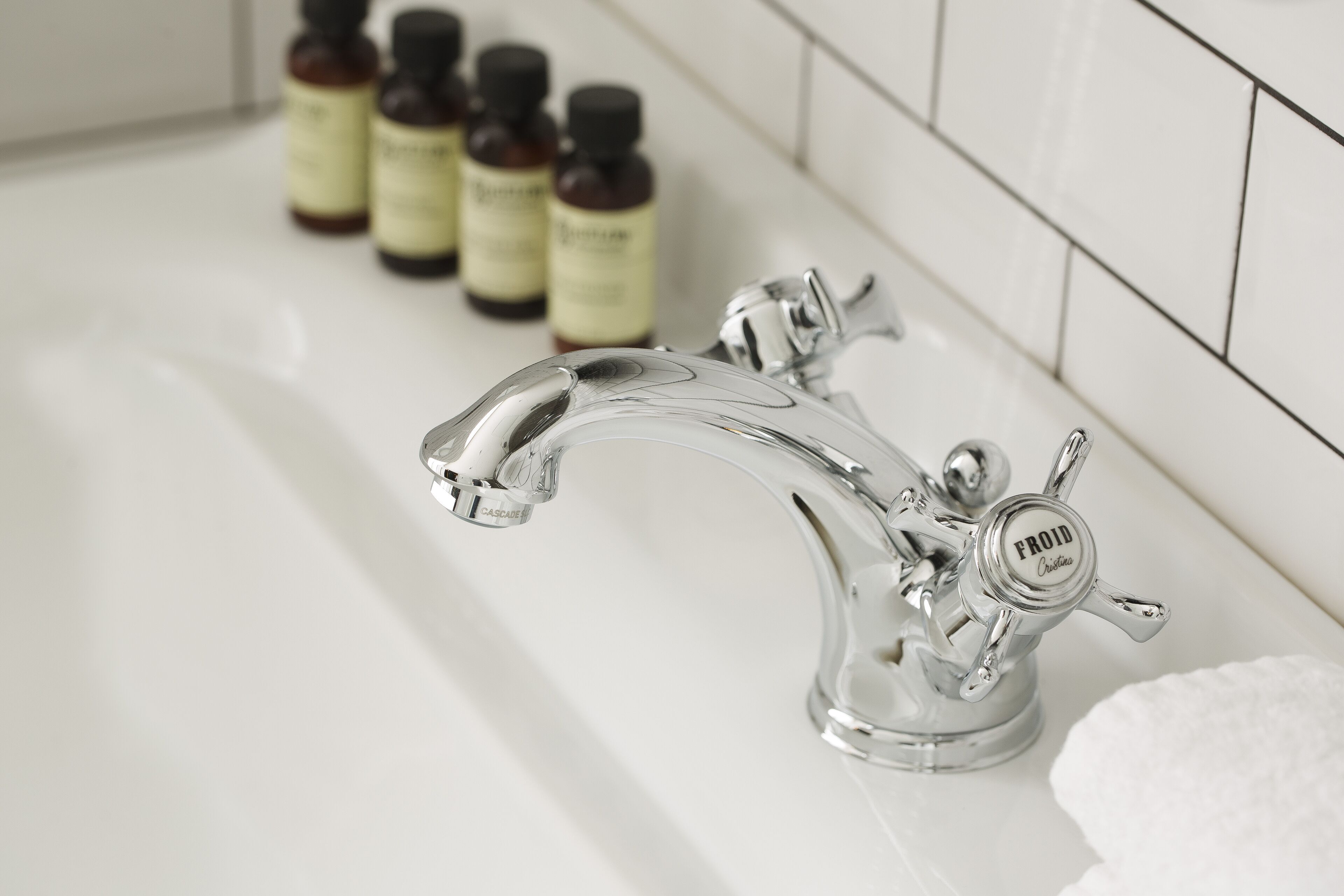 A bathroom with a chrome faucet labeled "FROID" and several small bottles of essential oils on the counter.