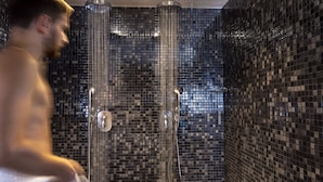Chuveiro com porta de vidro e parede revestida de azulejos.