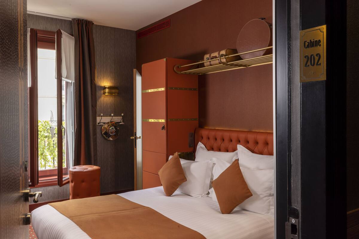 A hotel room with a bed, a wardrobe, a hanging luggage rack, and a door with a sign.