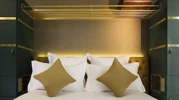 Una cama con ropa de cama blanca y dorada, un cabecero con una lámpara y una maleta sobre el cabecero.