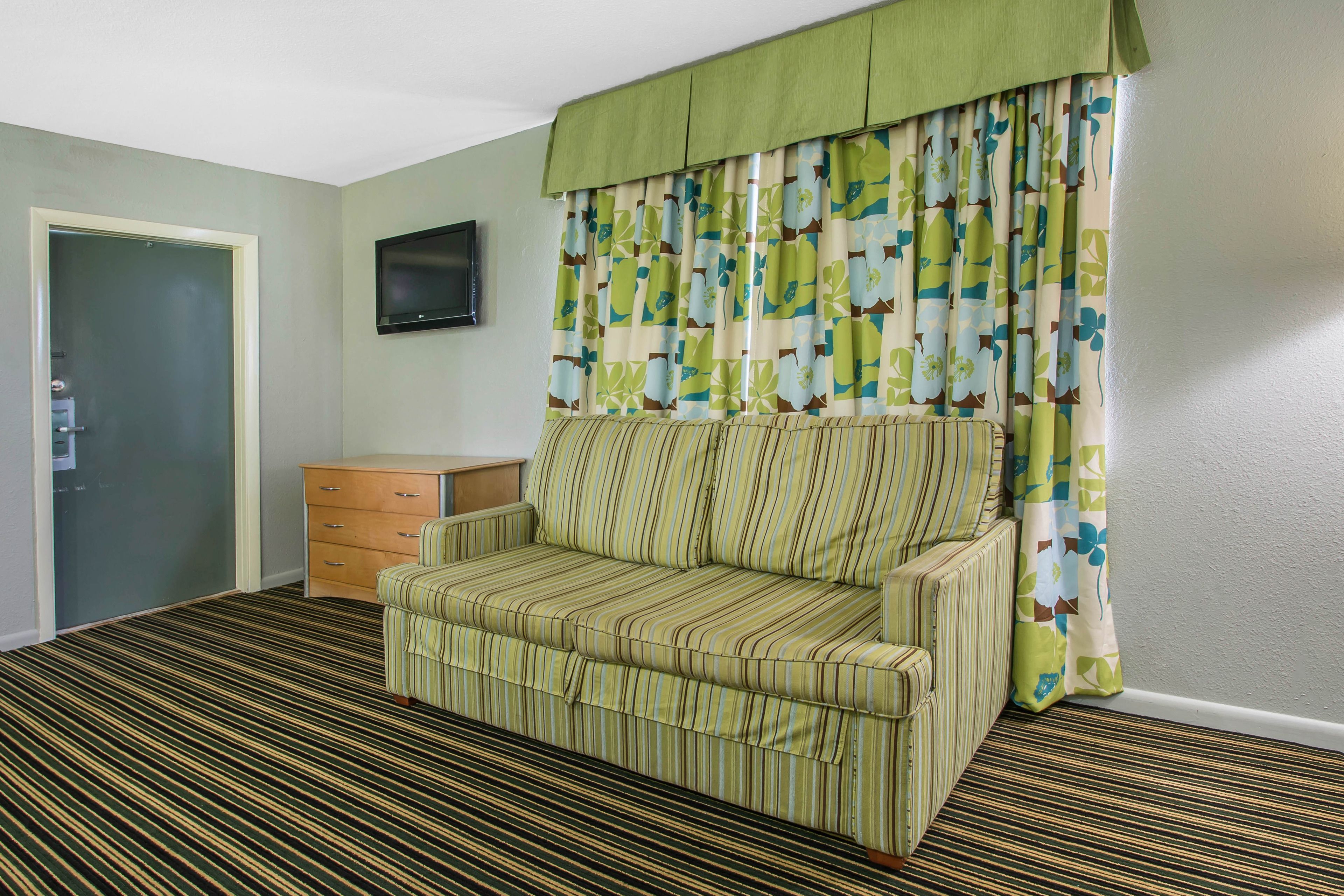 A room with a striped sofa, a wooden cabinet, a television on the wall, and a patterned curtain.