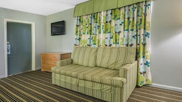 A room with a striped sofa, a wooden cabinet, a television on the wall, and a patterned curtain.