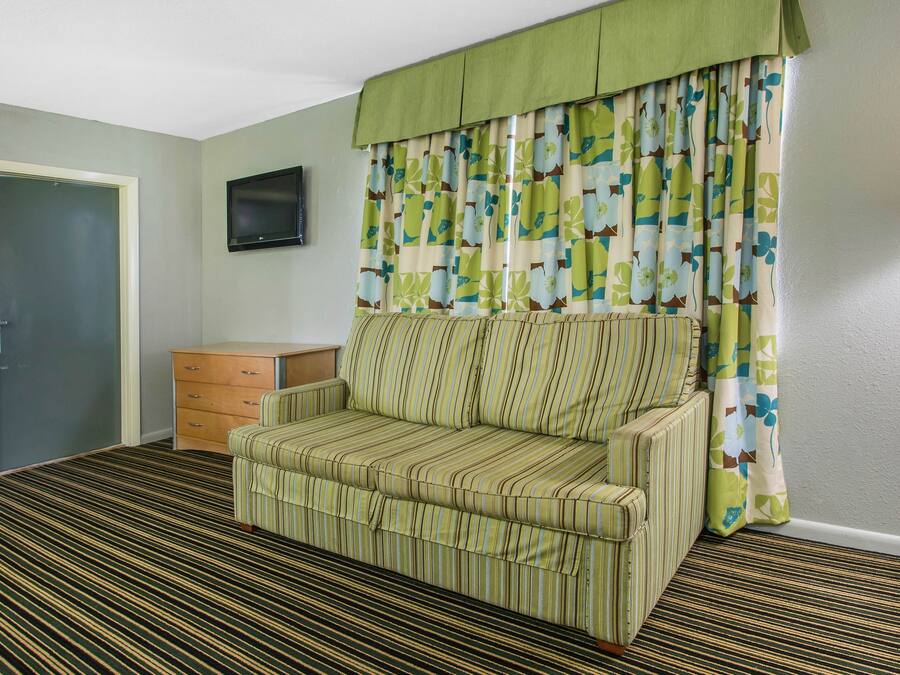 A room with a striped sofa, a wooden cabinet, a television on the wall, and a patterned curtain.