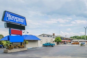 A motel with a sign reading "Rodeway Inn & Suites," a blue pickup truck parked in the lot, and a building with a blue roof.