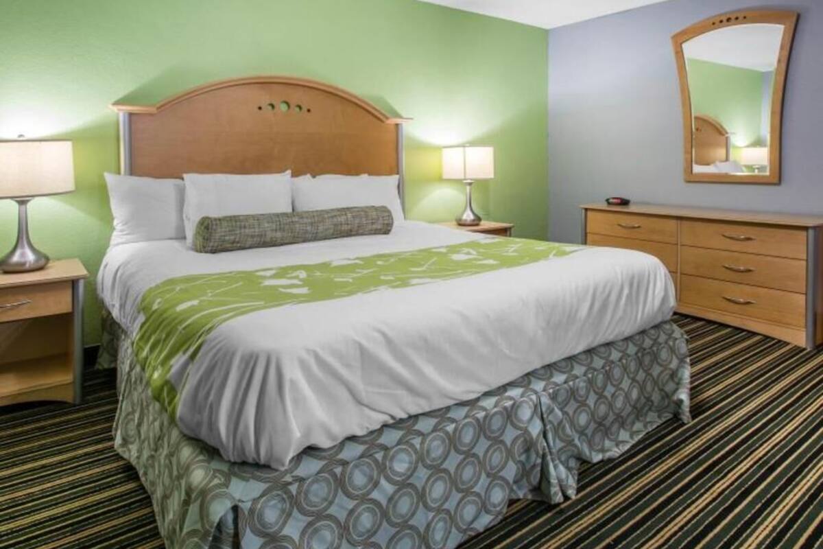 A hotel room with a bed, bedside tables, a dresser, a mirror, and a patterned carpet.