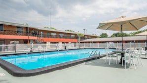 A swimming pool with a white fence, outdoor seating, and a building with balconies in the background.