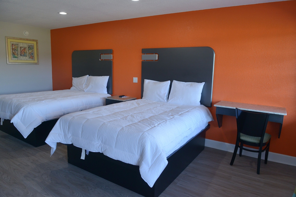 A hotel room with two beds, a desk, and a chair.