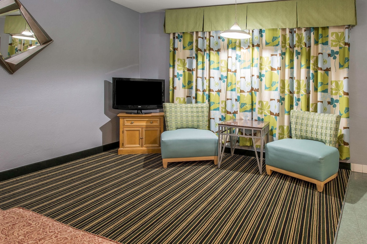 A hotel room with a television, two armchairs, a small table, and a patterned carpet.