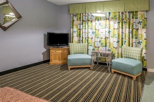 A hotel room with a television, two armchairs, a small table, and a patterned carpet.