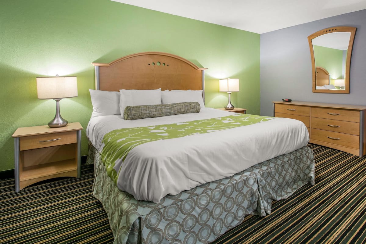 A neatly made bed with a wooden headboard, two bedside tables with lamps, a dresser, and a mirror on the wall.