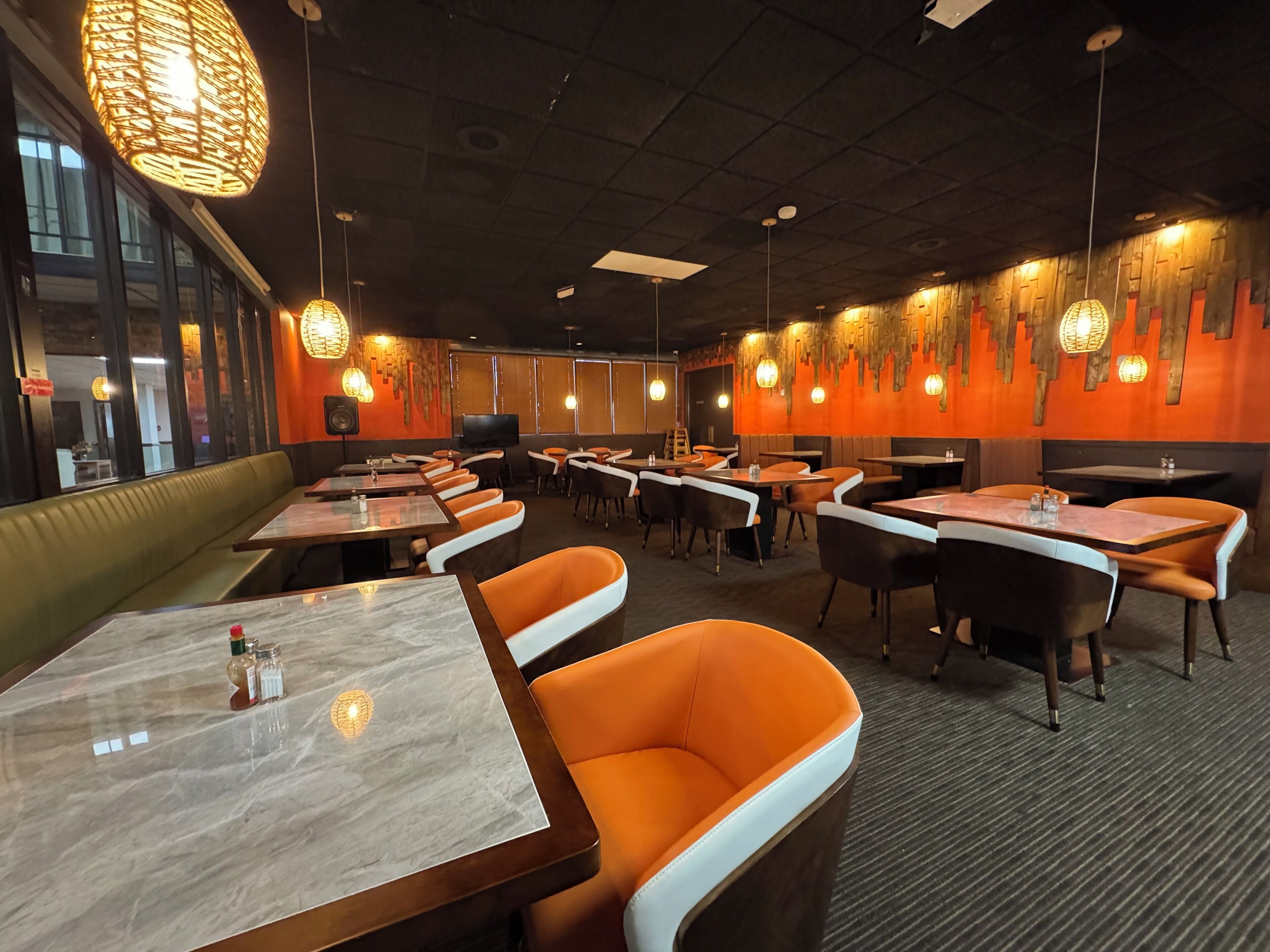 Een restaurantinterieur met zitjes, tafels, hangende lampen en een televisiescherm.