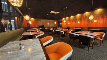 Een restaurantinterieur met zitjes, tafels, hangende lampen en een televisiescherm.