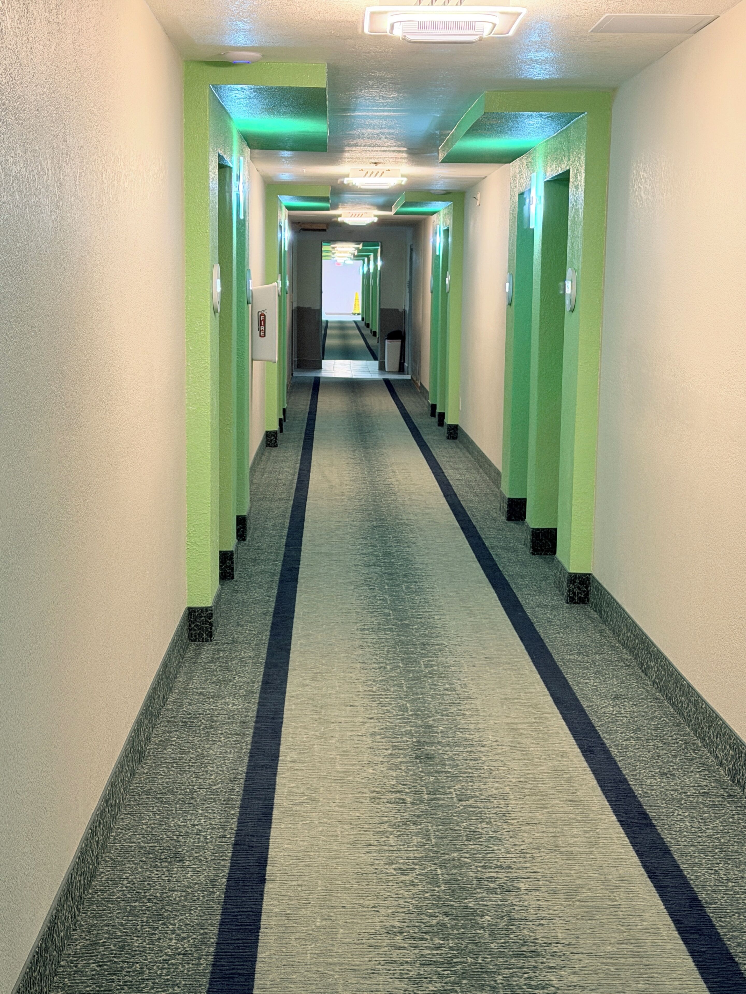 A long, narrow hallway with green walls and a carpeted floor, leading to a bright exit.