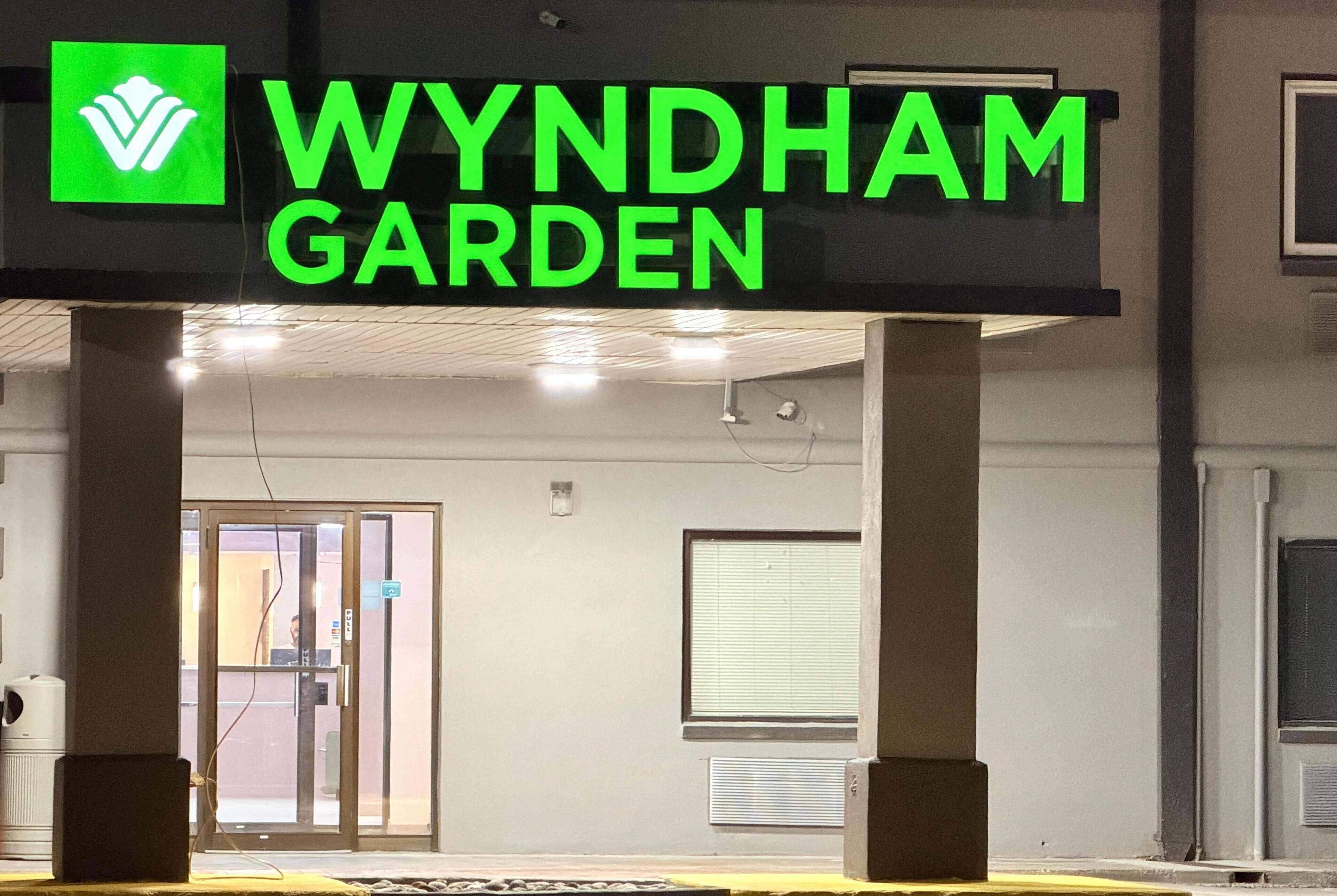 A sign for 'WYNDHAM GARDEN' with a logo, and a building entrance with a glass door and a window.