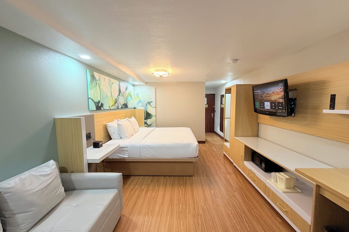Una habitació d'hotel amb un llit, un sofà, una televisió, una taula de treball i un mirall.